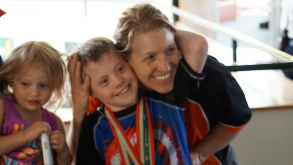 A female volunteer hugging a young male Special Olympics athlete who's just won a race.