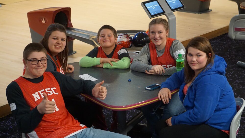 Gunner Sanderson and friends smiling together at a bowling alley.