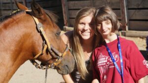 Miranda Breitag smiling with a young female Special Olympics athlete and a horse.