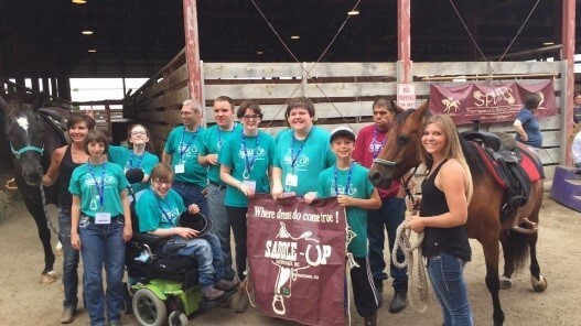 The Special Olympics equestrian team posting with a banner and horses.