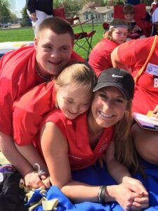 Coach Kaylee Schirado smiling and hugging two Special Olympics athletes.