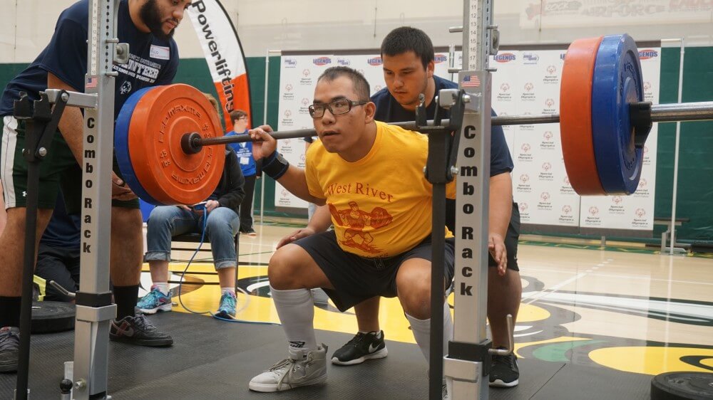 A coach helping a Special Olympics athlete lift weights.