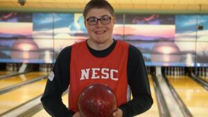 Gunner Sanderson smiling and holding a bowling ball in front of a bowling lane.