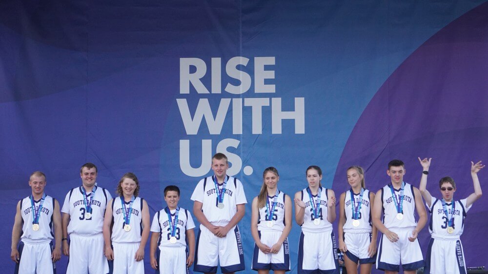 Members of the Unified Team standing in front of Rise with Us sign.